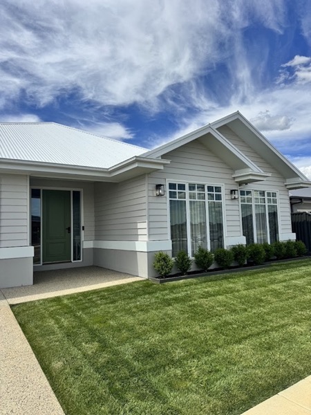 A pale weatherboard home with a metal roof and a mown front lawn