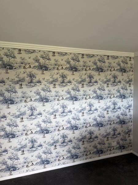 A bedroom wall hung with a blue and white bush scene wallpaper