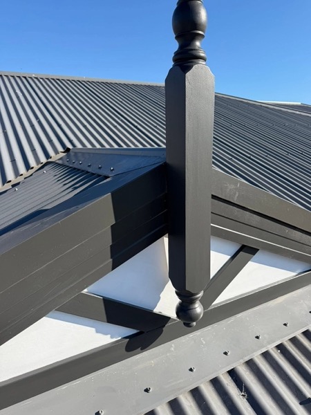 A dark metal roof with a painted timber finial at the ridge