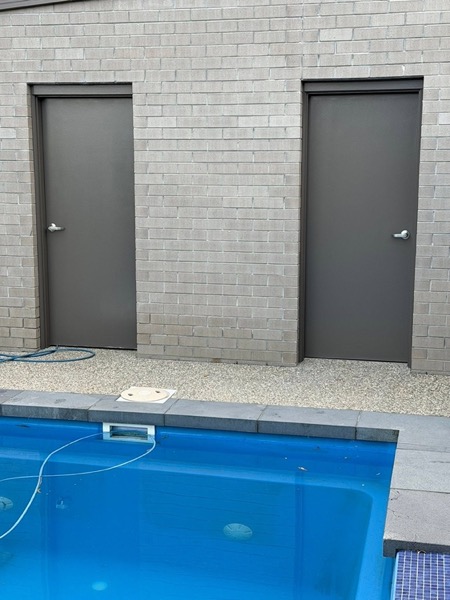 A grey painted brick wall with two grey doors, beside a pool