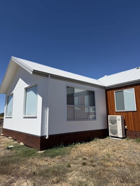 A white house with a brick base, a metal roof and a timber-clad corner