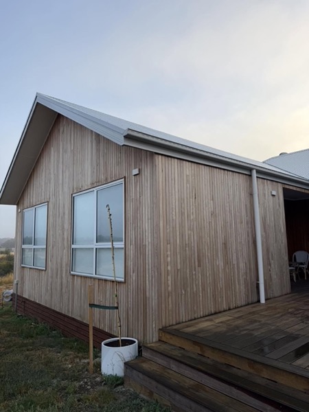 A timber-clad cabin with white window frames and a timber deck