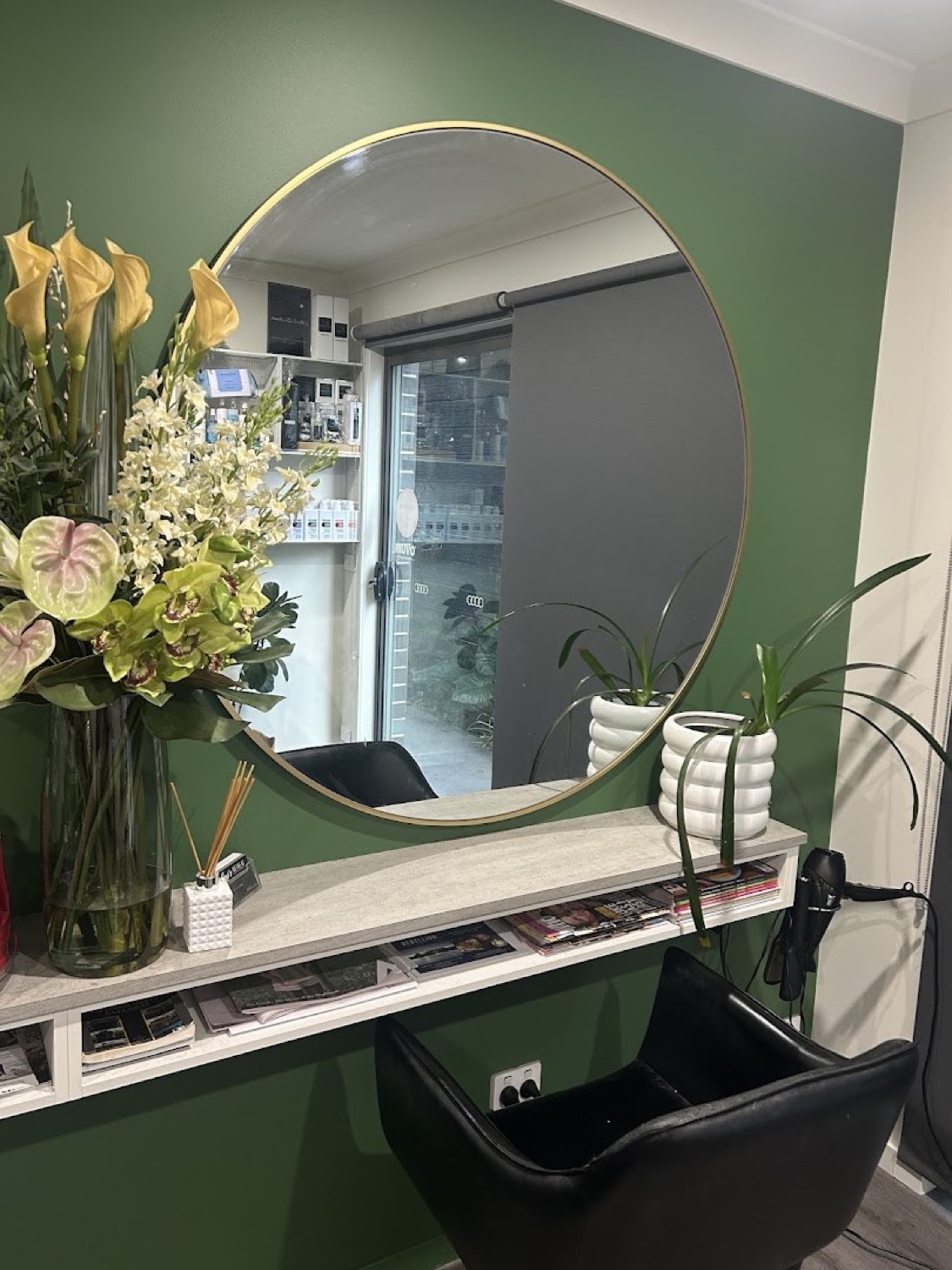 A deep green feature wall with a round mirror and a vase of flowers