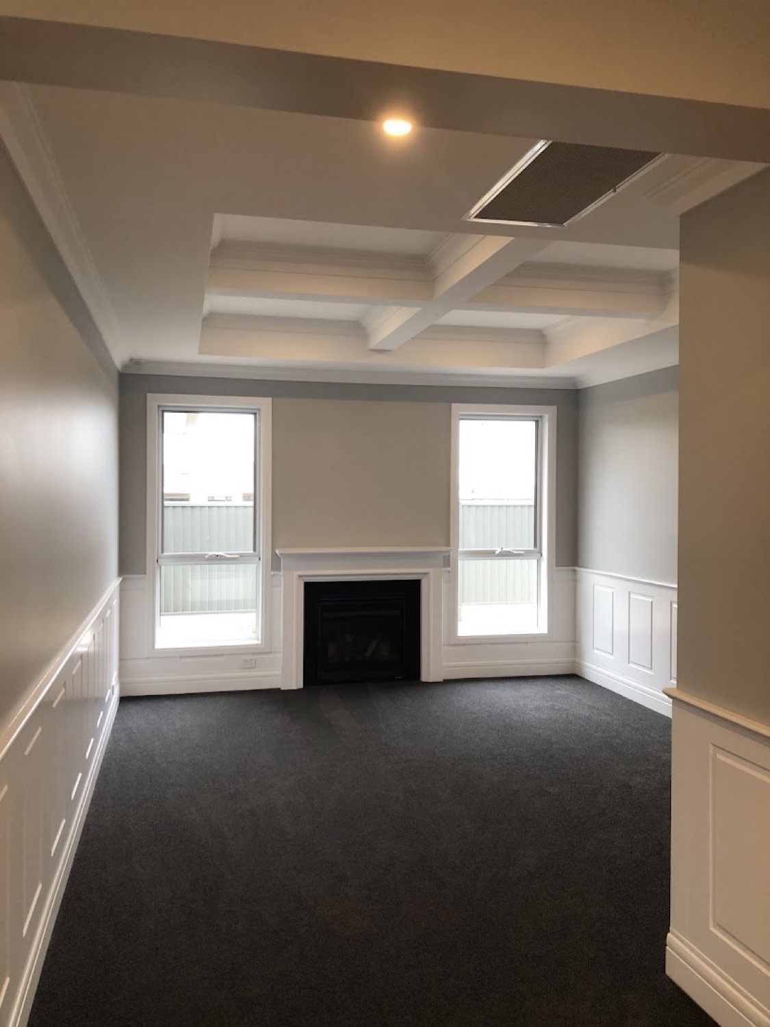 A living room with a coffered ceiling, panelled walls and a fireplace