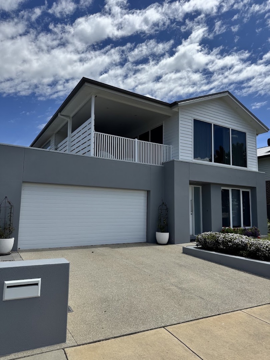 A two-storey home with grey cladding, a white garage door and a concrete driveway