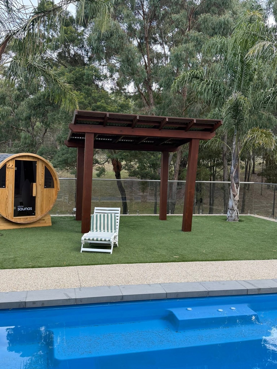 A timber pergola beside a pool with gum trees behind it