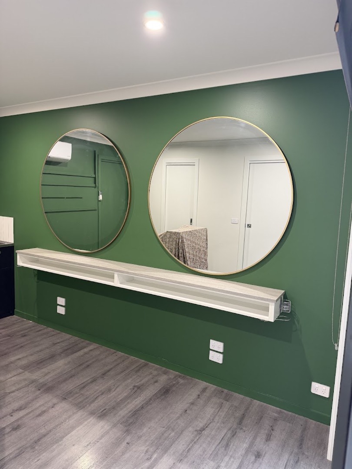 A deep green feature wall with two round mirrors above a timber shelf