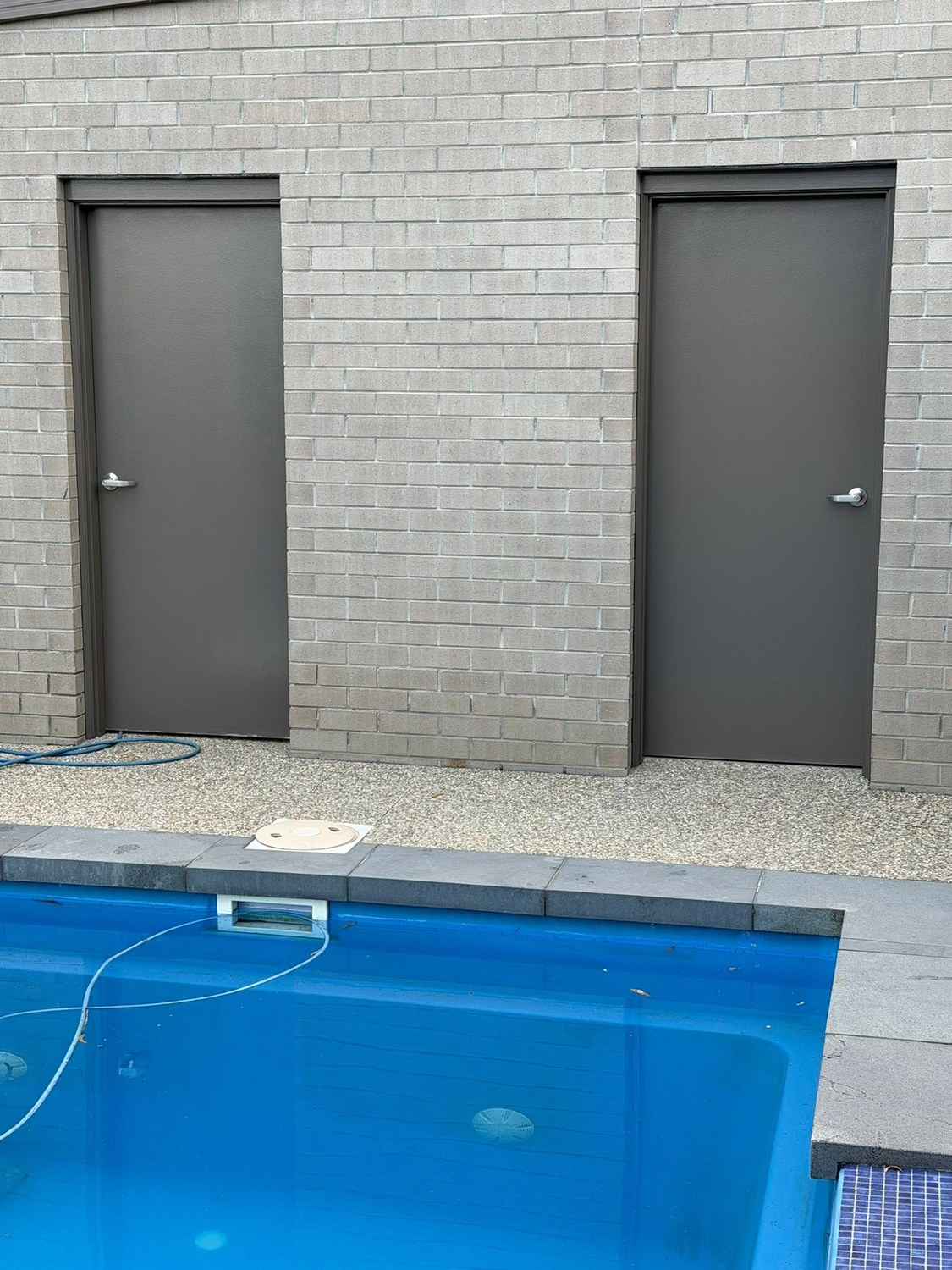 A grey painted brick wall with two grey doors, beside a pool